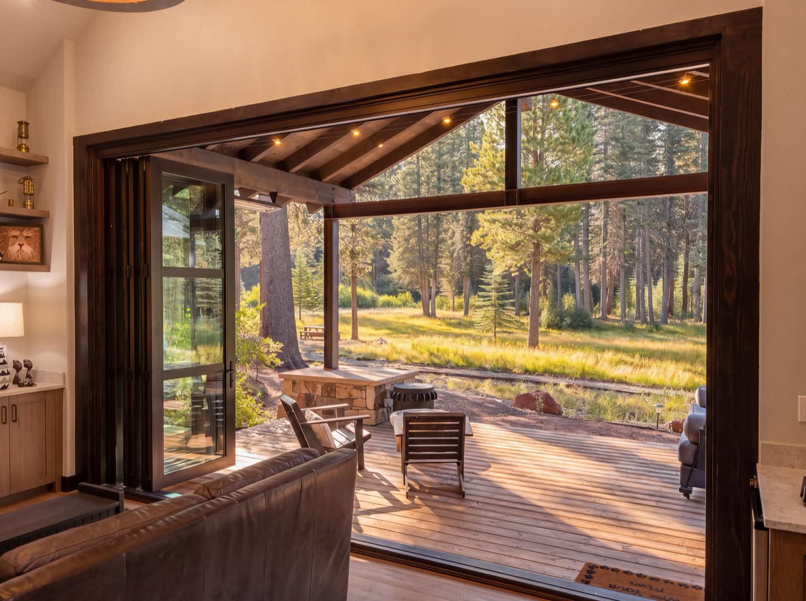 The lodge's folding glass walls open onto the porch and the riverside meadow at golden hour